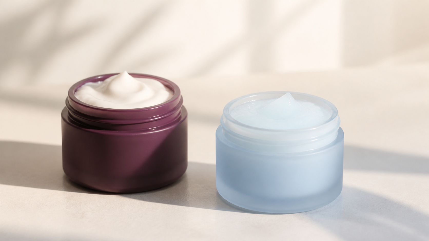 Editorial still life of two unbranded cream jars in plum and pale blue, illustrating a rich cream versus a water cream.